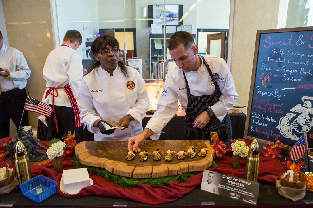 Beverly Boyd (left), protocol officer for Marine Forces Reserve, and Staff Sgt. Anthony Maietta (right), an enlisted aide to Lt. Gen. Rex C. McMillian, commander of MARFORRES and Marine Forces North, place food on a serving plate during the annual Best Chef Louisiana competition at the Lakefront Airport Terminal Building, New Orleans, April 10, 2018. The chefs event gives recognition to select chefs and honors them for their contribution to the New Orleans culinary scene and is also an opportunity for them to showcase their talent by serving a sampling of their signature dishes to the attendees.