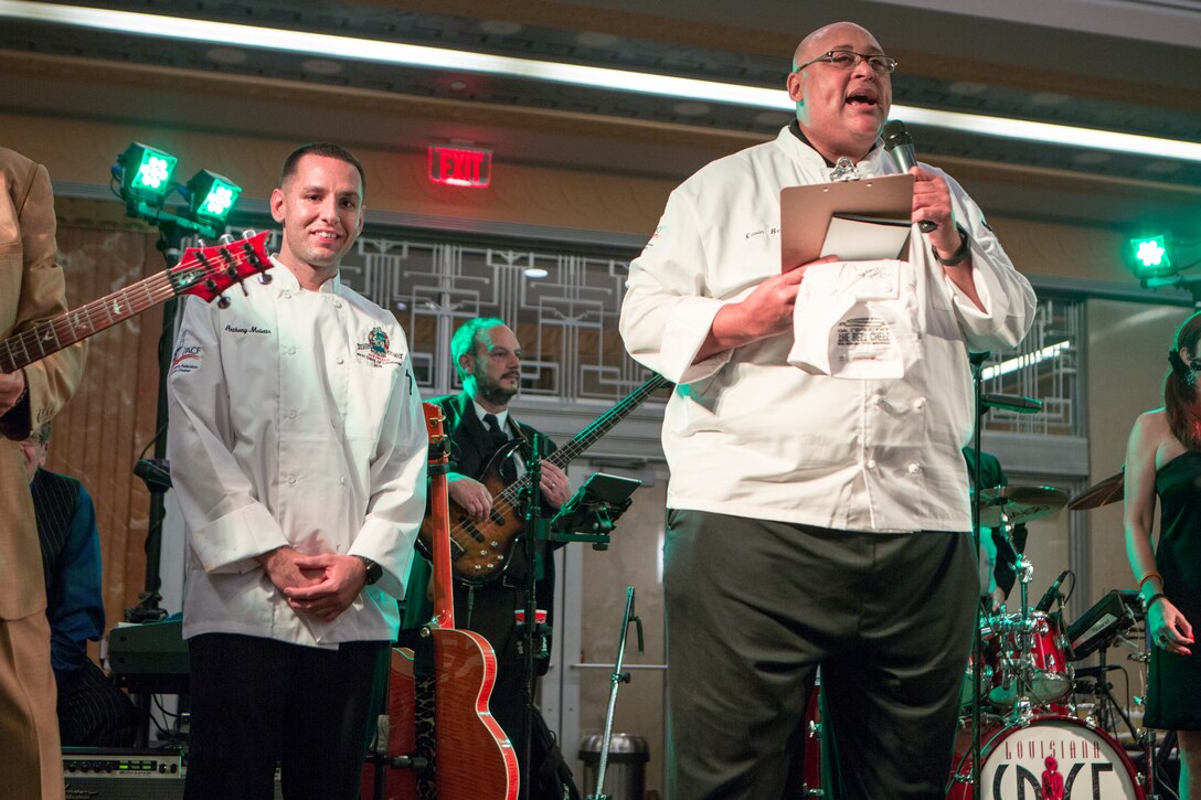 New Orleans celebrity chef Kevin Belton (right) announces Staff Sgt. Anthony Maietta (left), an enlisted aide to Lt. Gen. Rex C. McMillian, commander of Marine Forces Reserve and Marine Forces North, as the winner of the annual Best Chef Louisiana competition at the Lakefront Airport Terminal Building, New Orleans, April 10, 2018. Maietta competed in the competition for the opportunity to showcase the Marine Corps in the New Orleans community, himself and one of his signature dishes.