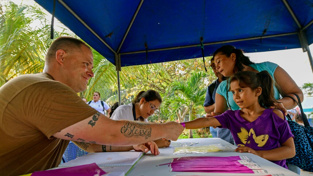 A sailor reaches across a table and shakes a little girl's hand.