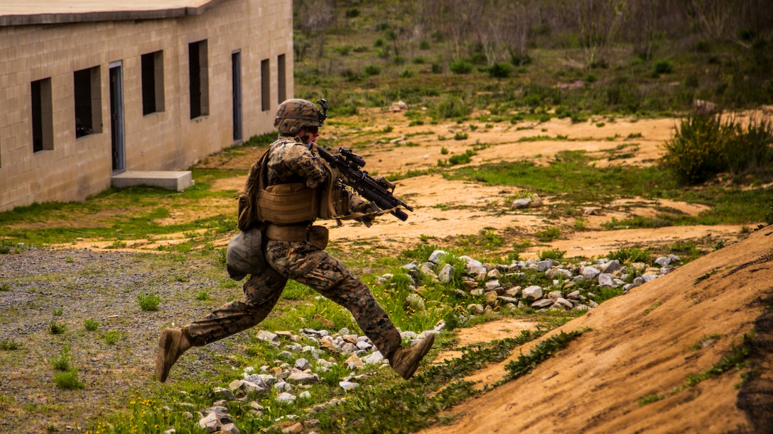 A Marine holding a weapon runs toward a hill.