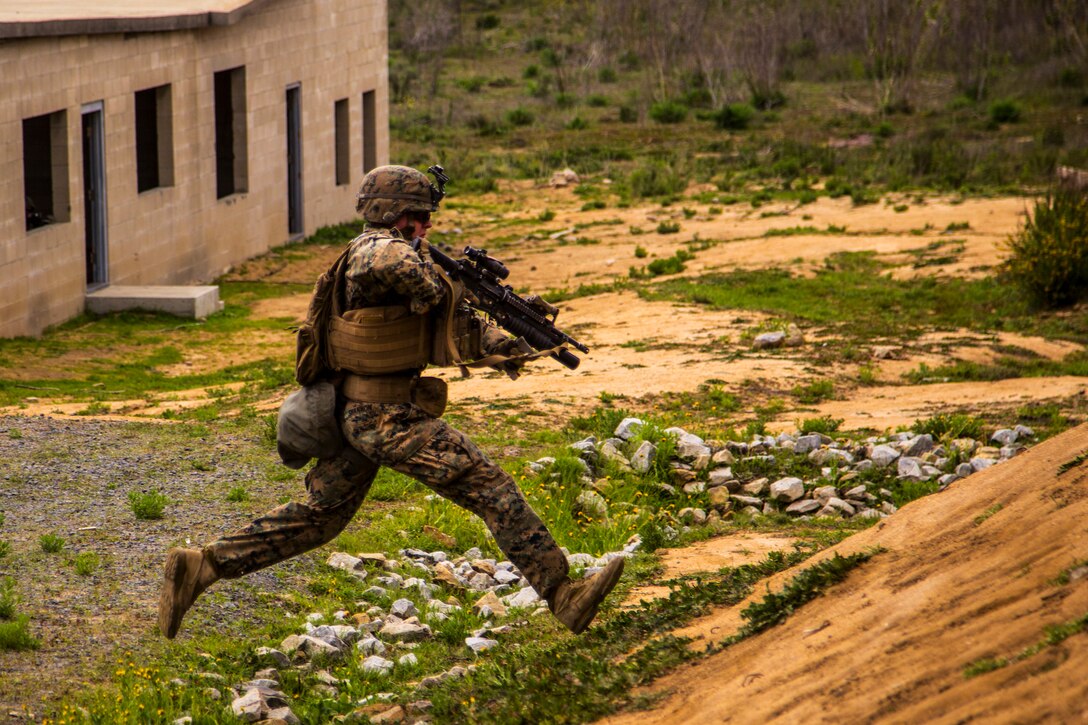 A Marine holding a weapon runs toward a hill.