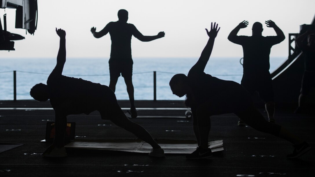 Four sailors, shown in silhouette, exercise on a ship with water in the background.