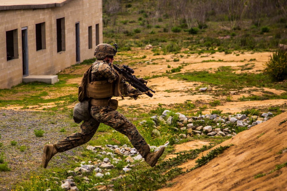 A Marine holding a weapon runs toward a hill.