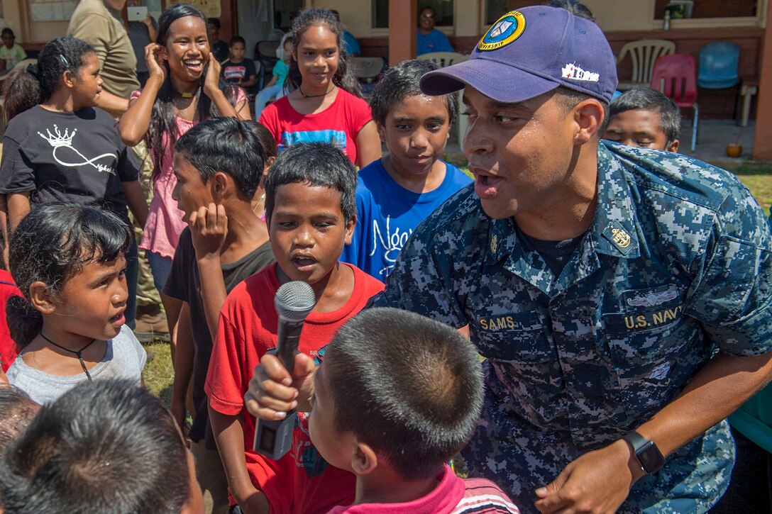 A sailor sings with a group of children.