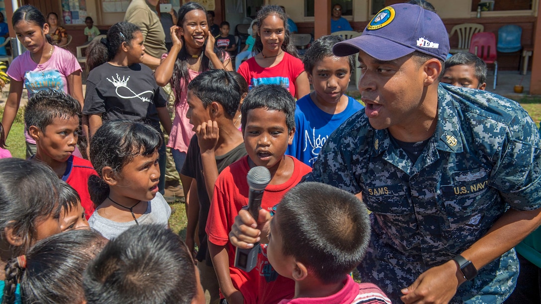 A sailor sings with a group of children.