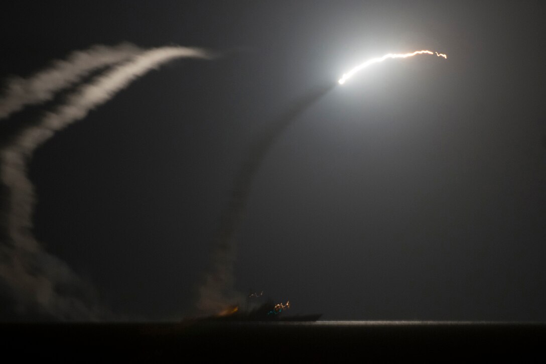 A missile launches on a curved trajectory from a ship traveling at night.