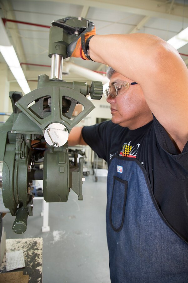 Mike Dokie, Optics Lab journeyman, demonstrates the detailed and very specific calibrations done on the M777 Howitzer optics equipment on an adjustable table mounted testing unit in their Optics Lab at Production Plant Barstow, Marine Depot Maintenance Command on the Yermo Annex aboard Marine Corps Logistics Base Barstow, Calif., March 28. Once the optical equipment is mounted, the team ensures that the calibrations allow for precision maneuvaring, tracking and firing of ammunition.