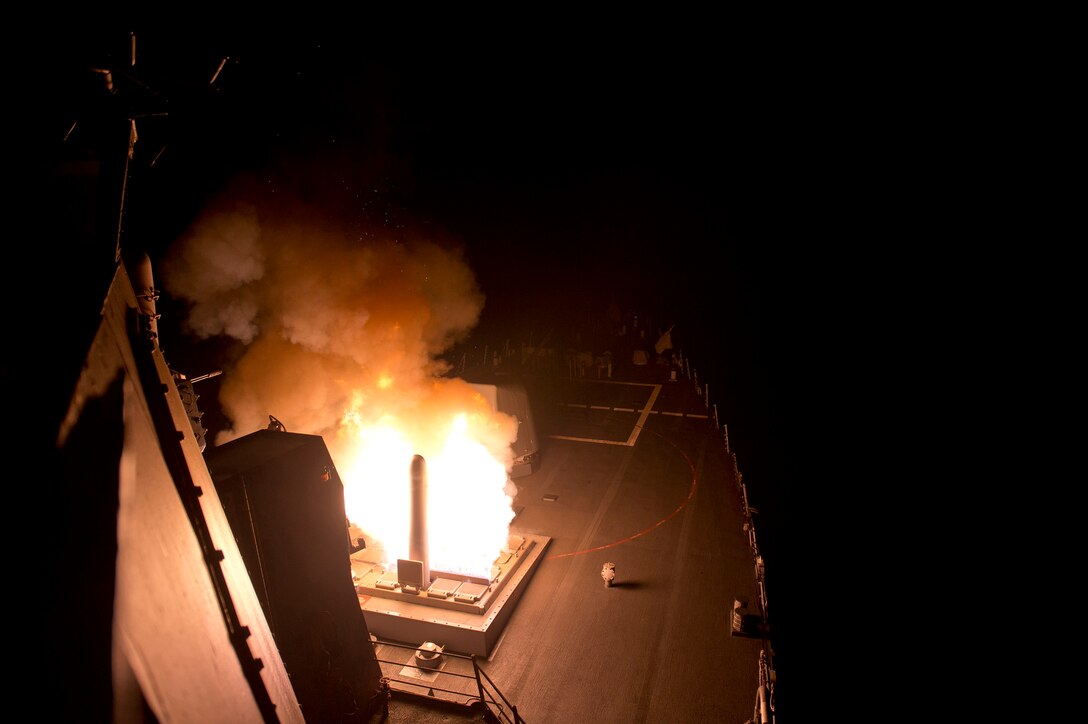A missile starts to launche from a ship at night, creating a ball of fire and smoke.