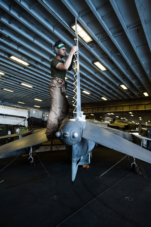 U.S. Marine Corps Staff Sgt. Johnathan B. Davis, the AV-8B Harrier airframes chief assigned to Marine Medium Tiltrotor Squadron (VMM) 162 (Reinforced), 26th Marine Expeditionary Unit (MEU), and a Mattoon, Illinois native, applies masking tape to the tail of an AV-8B Harrier prior to painting in the hangar deck of the Wasp-class amphibious assault ship USS Iwo Jima (LHD 7), April 11, 2018. The 26th MEU trains to sustain expeditionary readiness across a range of critical capabilities both afloat and ashore in order to be prepared to respond to crisis in the U.S. 5th Fleet Area of Operations. (U.S. Marine Corps photo by Cpl. Jered T. Stone/Released)