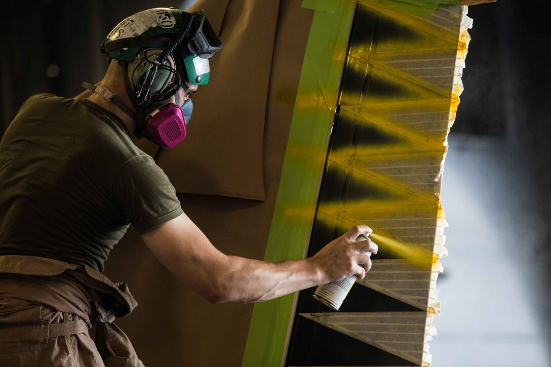 U.S. Marine Corps Staff Sgt. Johnathan B. Davis, the AV-8B Harrier airframes chief assigned to Marine Medium Tiltrotor Squadron (VMM) 162 (Reinforced), 26th Marine Expeditionary Unit (MEU), and a Mattoon, Illinois native, applies spray paint to the tail of an AV-8B Harrier in the hangar deck of the Wasp-class amphibious assault ship USS Iwo Jima (LHD 7), April 11, 2018. The 26th MEU trains to sustain expeditionary readiness across a range of critical capabilities both afloat and ashore in order to be prepared to respond to crisis in the U.S. 5th Fleet Area of Operations. (U.S. Marine Corps photo by Cpl. Jered T. Stone/Released)