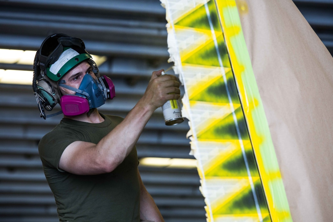 U.S. Marine Corps Staff Sgt. Johnathan B. Davis, the AV-8B Harrier airframes chief assigned to Marine Medium Tiltrotor Squadron (VMM) 162 (Reinforced), 26th Marine Expeditionary Unit (MEU), and a Mattoon, Illinois native, applies spray paint to the tail of an AV-8B Harrier in the hangar deck of the Wasp-class amphibious assault ship USS Iwo Jima (LHD 7), April 11, 2018. The 26th MEU trains to sustain expeditionary readiness across a range of critical capabilities both afloat and ashore in order to be prepared to respond to crisis in the U.S. 5th Fleet Area of Operations. (U.S. Marine Corps photo by Cpl. Jered T. Stone/Released)