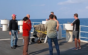 Maj. Christina Light (in red), Technical Operations Squadron Director of Operations with the Air Force Technical Applications Center, Patrick AFB, Fla., receives a briefing from Sean Kelly, the Ship's Operations Manager, for an upcoming balloon calibration sphere launch.