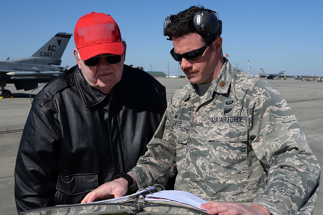 Two men look over some paperwork at an airfield.