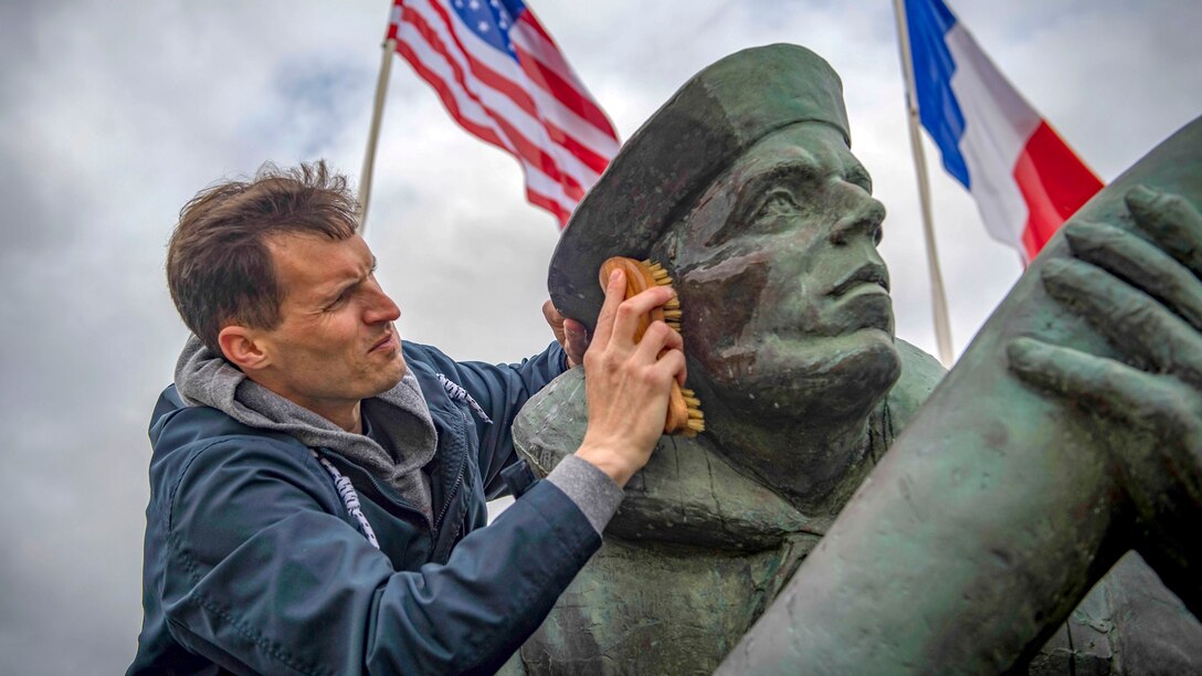 A sailor scrubs the face of statue with a brush, as U.S. and Fru