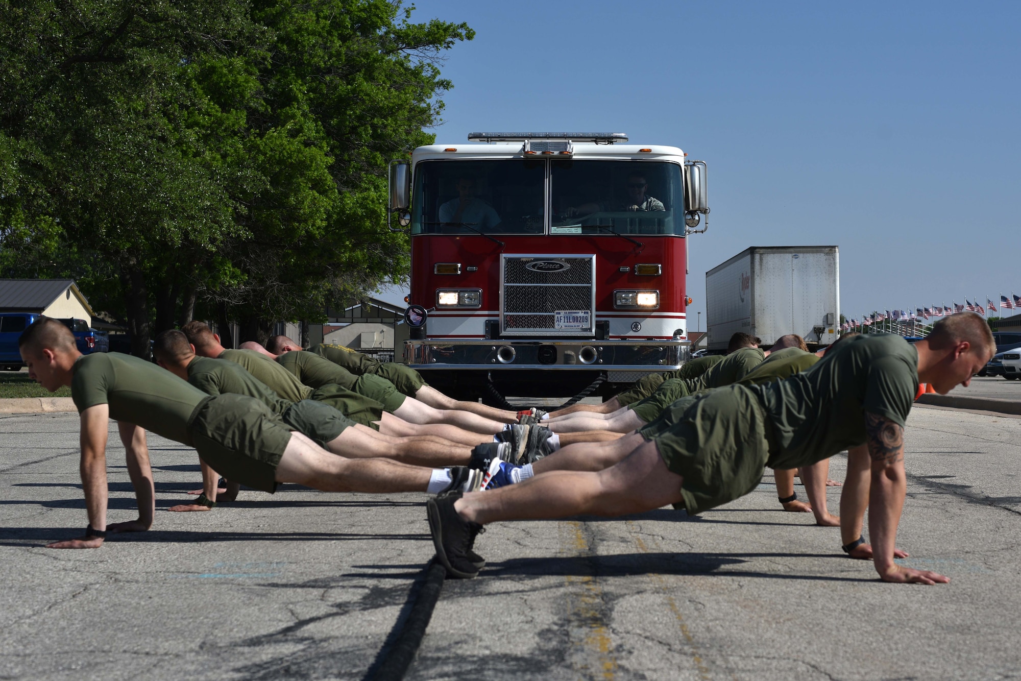 Marines from the Marine Detachment on Goodfellow hold a push-up position before pulling a firetruck during Sports Day at the Mathis Fitness Center on Goodfellow Air Force Base, Texas, April 13, 2018. Teams worked together to pull the firetruck across the line as quickly as possible.