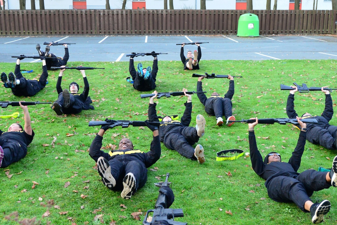 Rows of soldiers lie on the grass and hold their rifles and legs up.