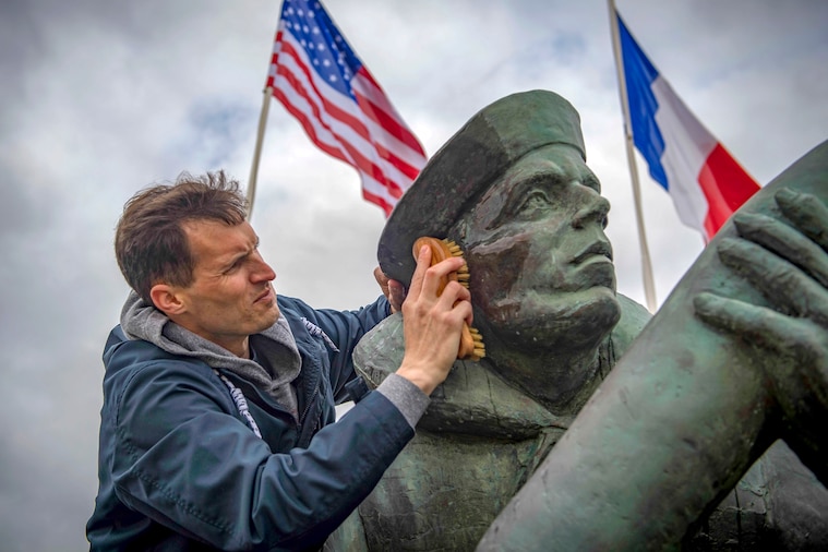 A sailor scrubs the face of statue with a brush, as U.S. and Fru