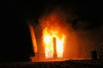 A missile surrounded by flames launches from a ship at night.