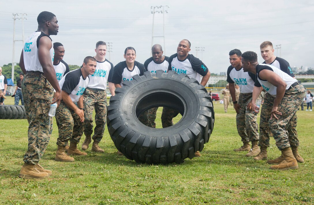 U.S. Marine Cpl. Hanah Ogden, center-left, and U.S. Marine 2nd Lt. Edward Robinson, center-right, flip a tire against the Army team at the 3rd Annual Sexual Assault Awareness and Prevention Month Field Meet April 13, 2018, at Camp Foster, Okinawa, Japan. The Single Marine Program provided music and the Firefighters Association made breakfast and lunch for the Marines, Sailors, Airmen and Soldiers participating in the field meet. III Marine Expeditionary Force hosted this year’s joint service event to raise awareness throughout the branches about sexual assault and to build a sense of unity through competition.  Ogden is a native of Buffalo, New York and a legal/administration clerk with Combat Logistics Regiment 4, 3rd Marine Logistics Group. Robinson is a native of Chesapeake, Virginia and a platoon commander with Transportation Services, CLB-4, 3rd MLG. (U.S. Marine Corps photo by Lance Cpl. Isabella Ortega)