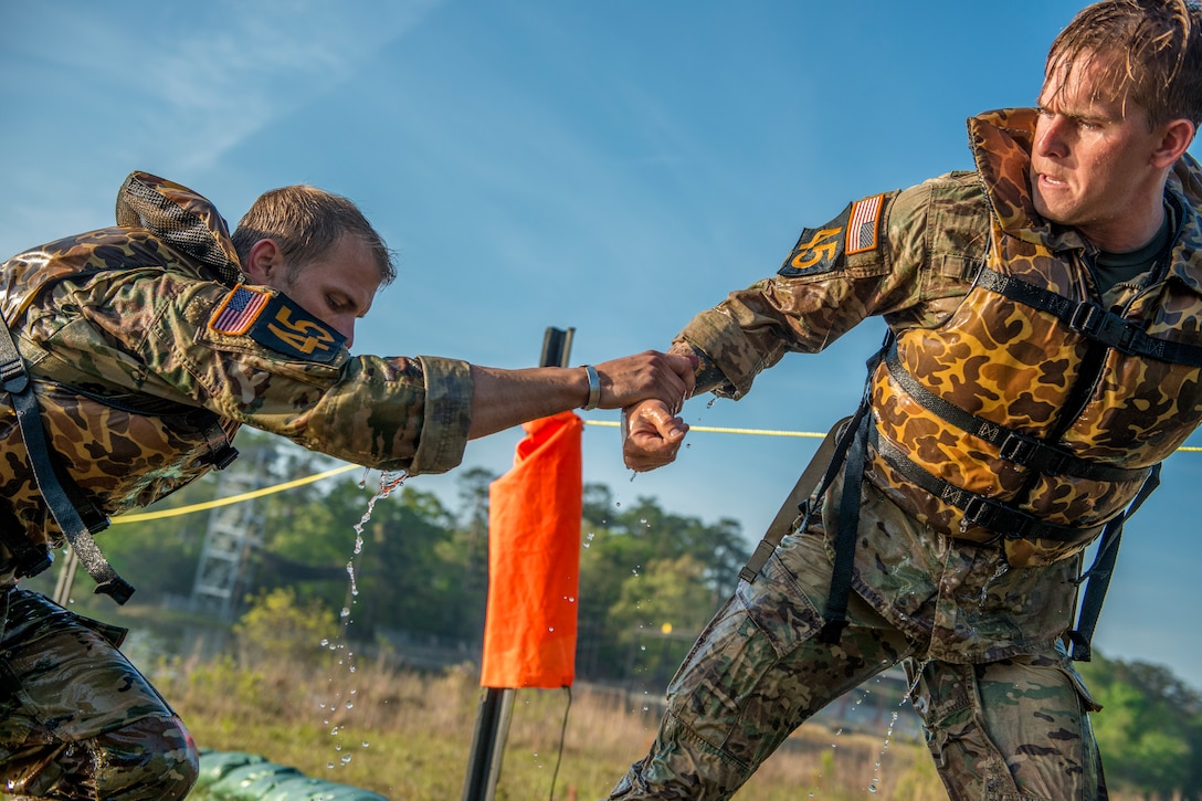 One soldier reaches out to help another soldier.