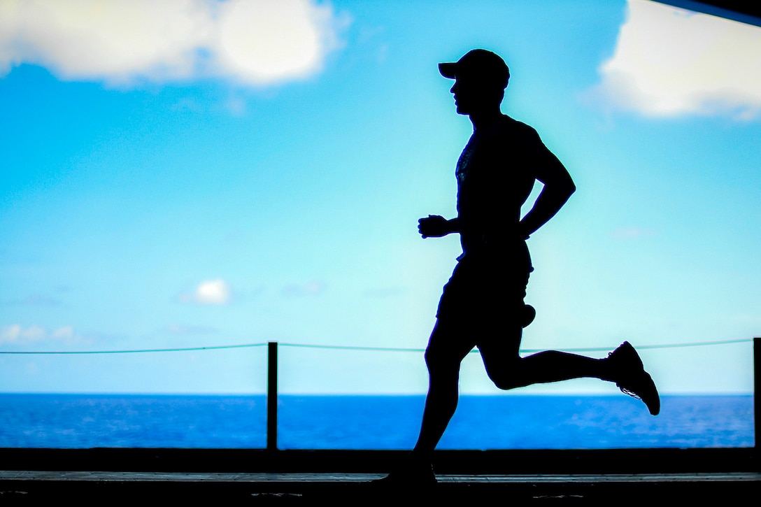 A sailor runs on a ship with water and sky in the background.