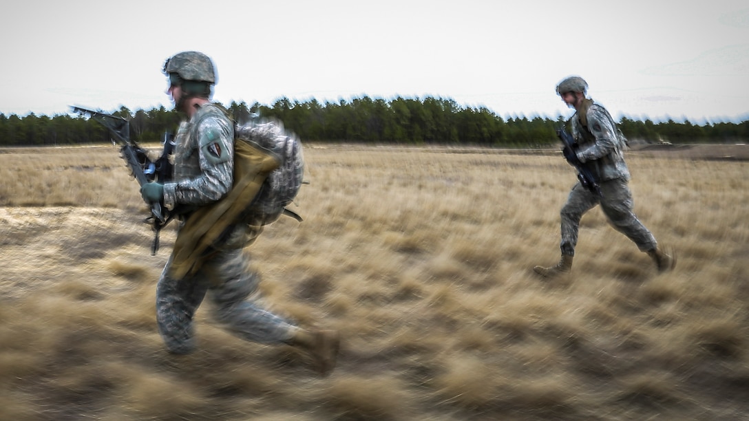 Two soldiers run through a field.