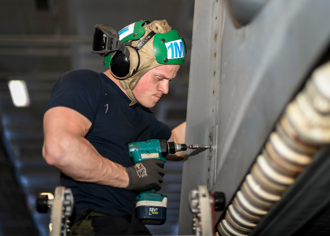 A sailor screws in brackets on the wing of the plane.