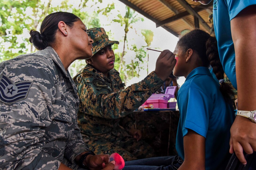 An airman helps paint a face of a child.