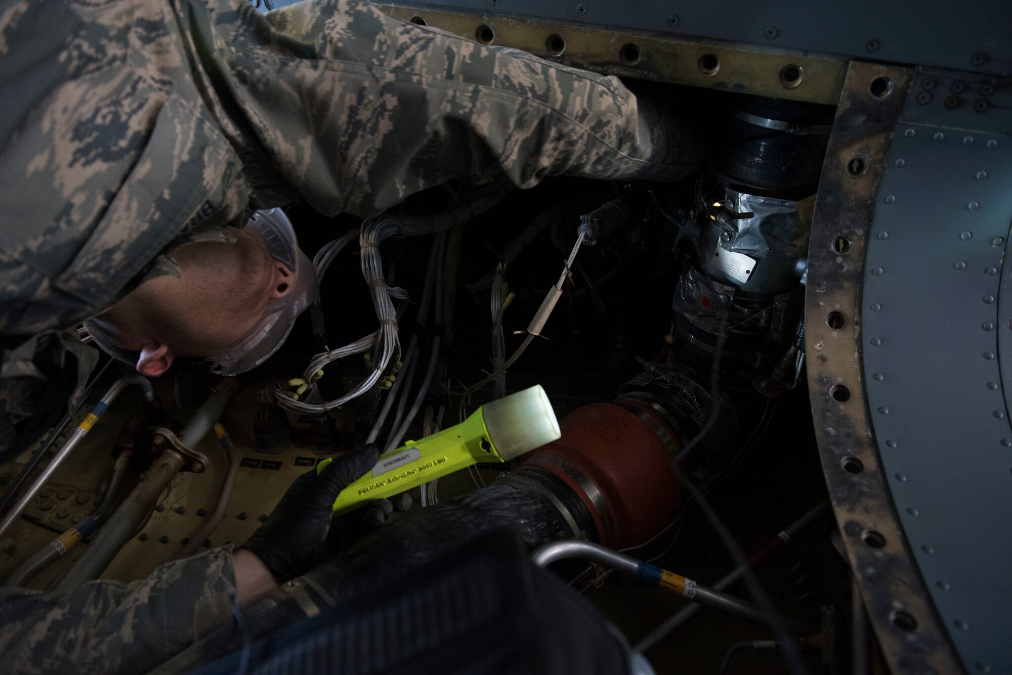An Airmen uses a flashlight to look at an aircraft part.