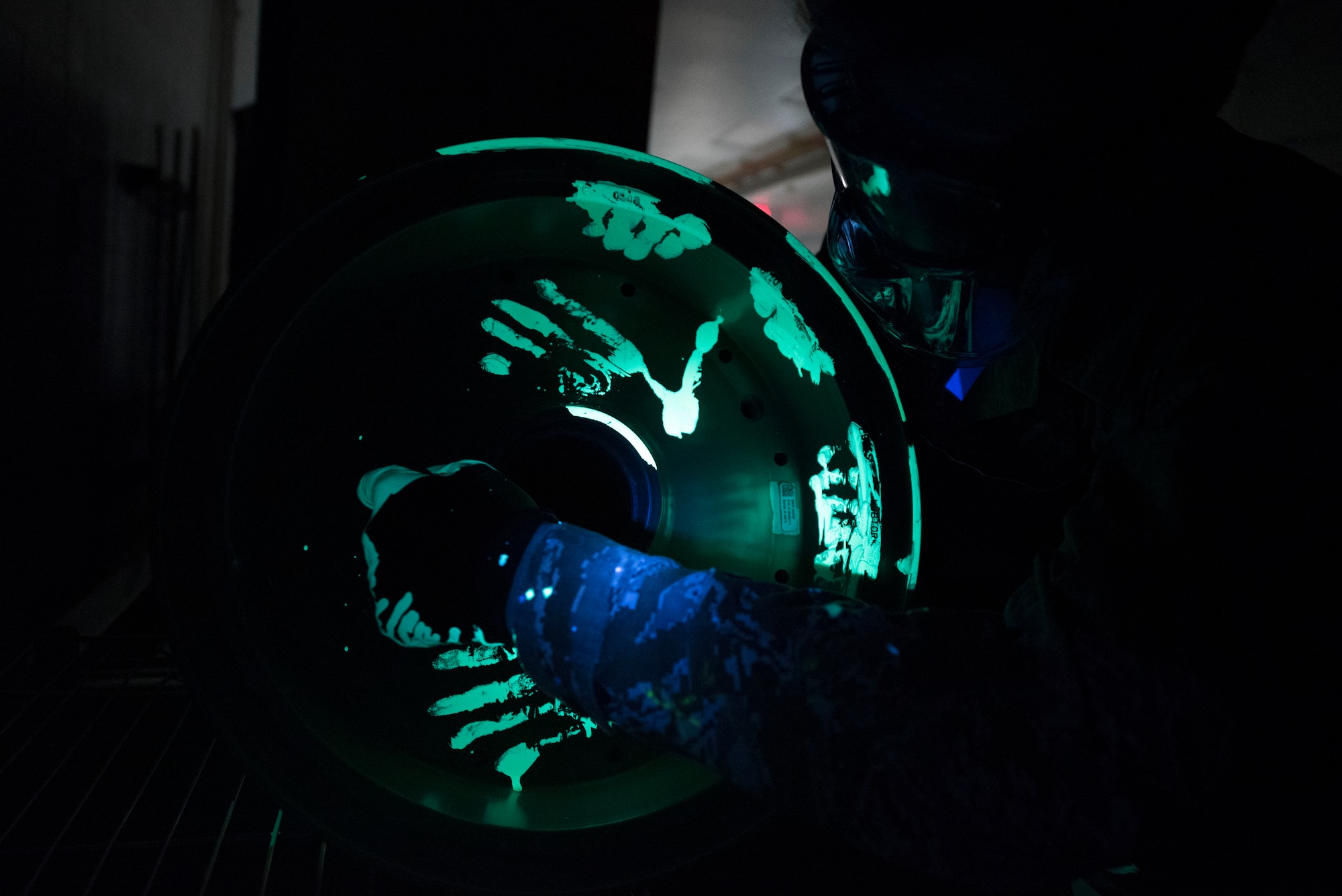 Man puts glowing liquid penetrant on aircraft wheel.