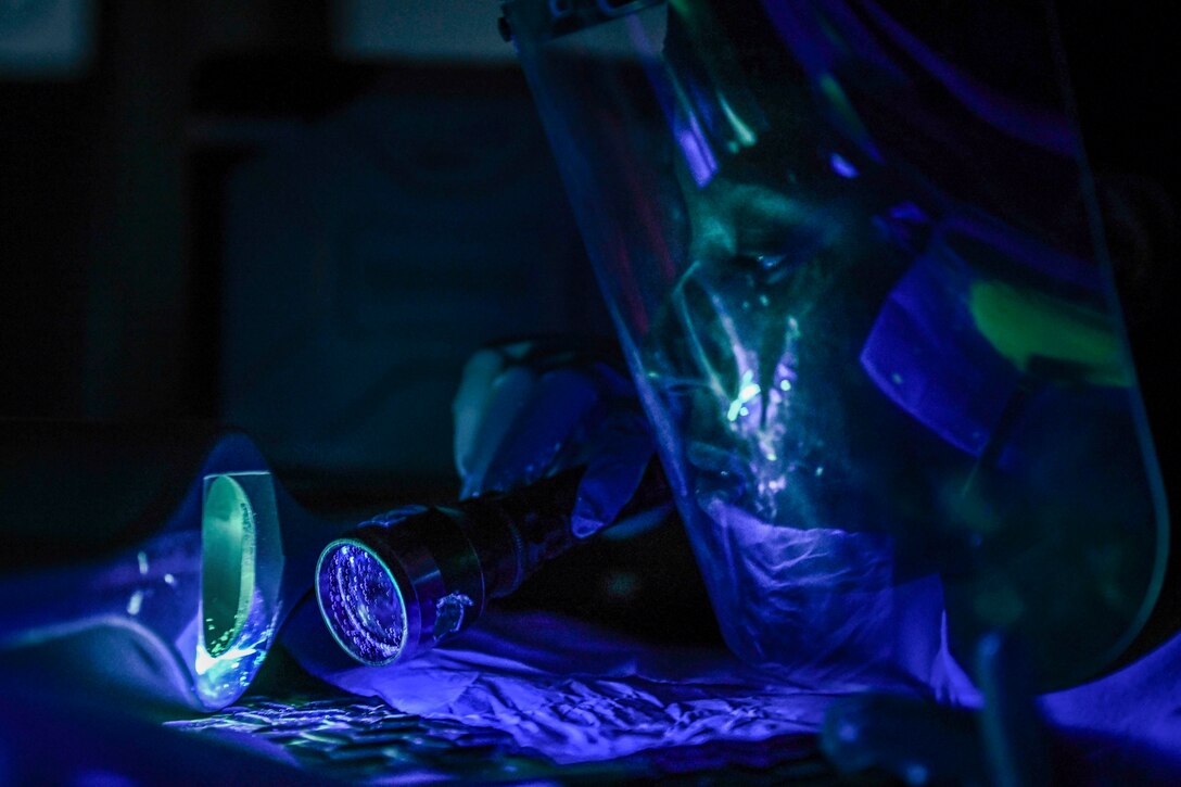 An airman uses a blue light to look at a surface.