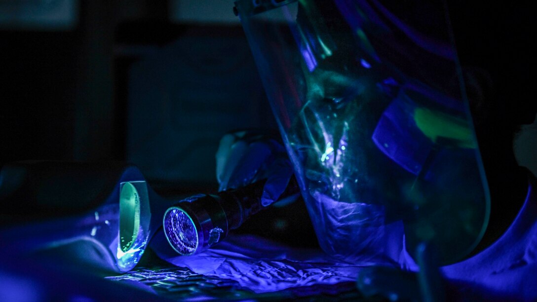 An airman uses a blue light to look at a surface.
