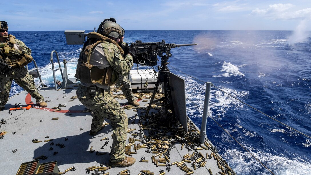 A sailor shoots a gun toward water.