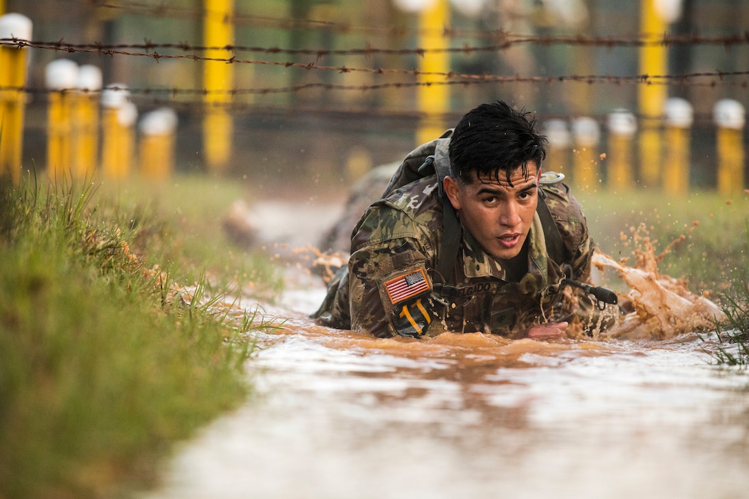 A soldier crawls through the mud below wires.