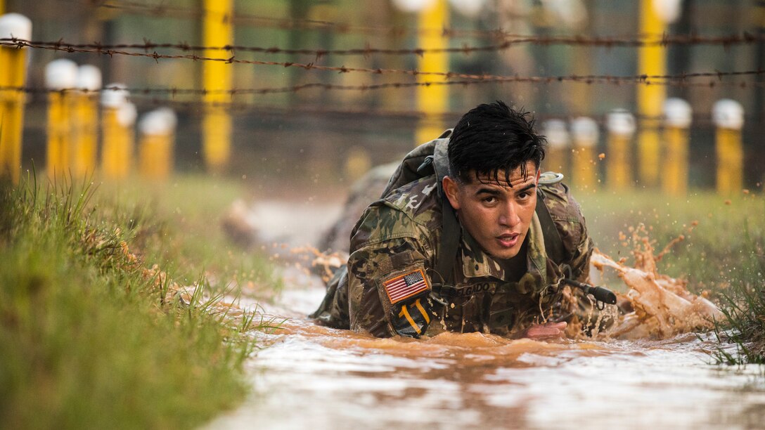 A soldier crawls through the mud below wires.