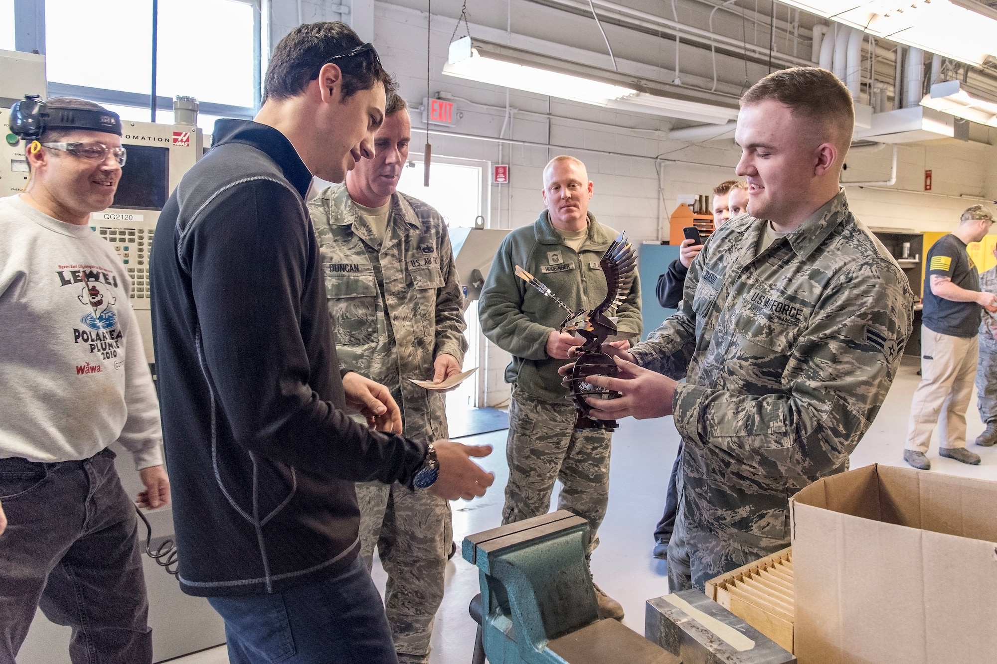 Airman 1st Class Lance Kielbaso, 436th Maintenance Squadron aircraft metals technology apprentice, presents Joey Logano, driver of the No. 22 Ford in the Monster Energy NASCAR Cup Series, with an eagle manufactured at the fabrication flight facilities April 11, 2018, at Dover Air Force Base, Del. The eagle was cut from scrap stainless steel using a Computer Numerical Controlled (CNC) machining tool and tack welded together. (U.S. Air Force photo by Roland Balik)