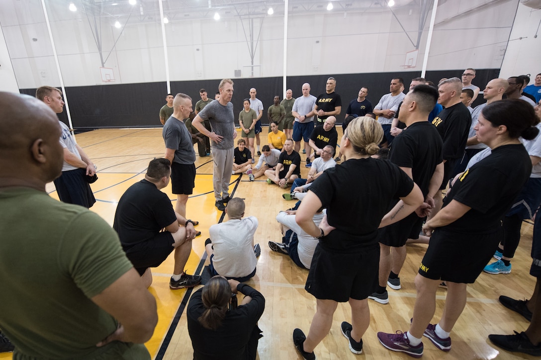 Defense leaders speak to troops in a gym during a physical training session.