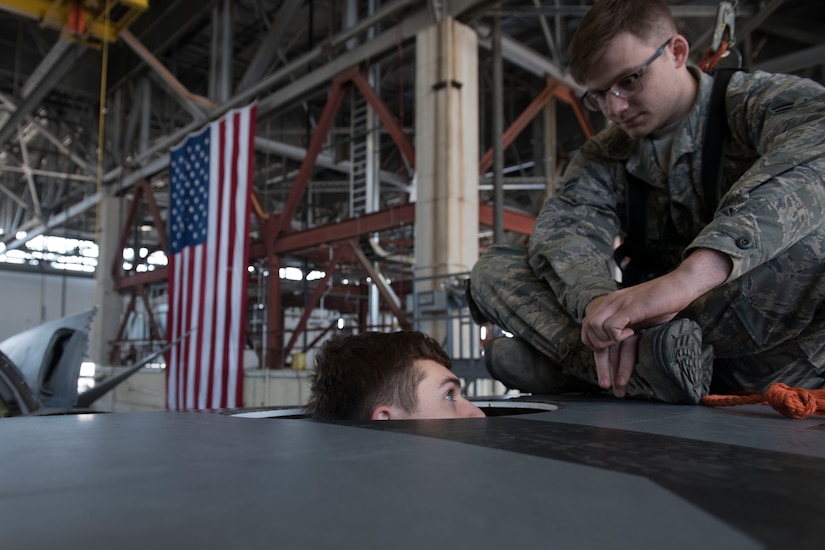 An Airmen looks down at another Airmen who is in the wing of an aircraft.