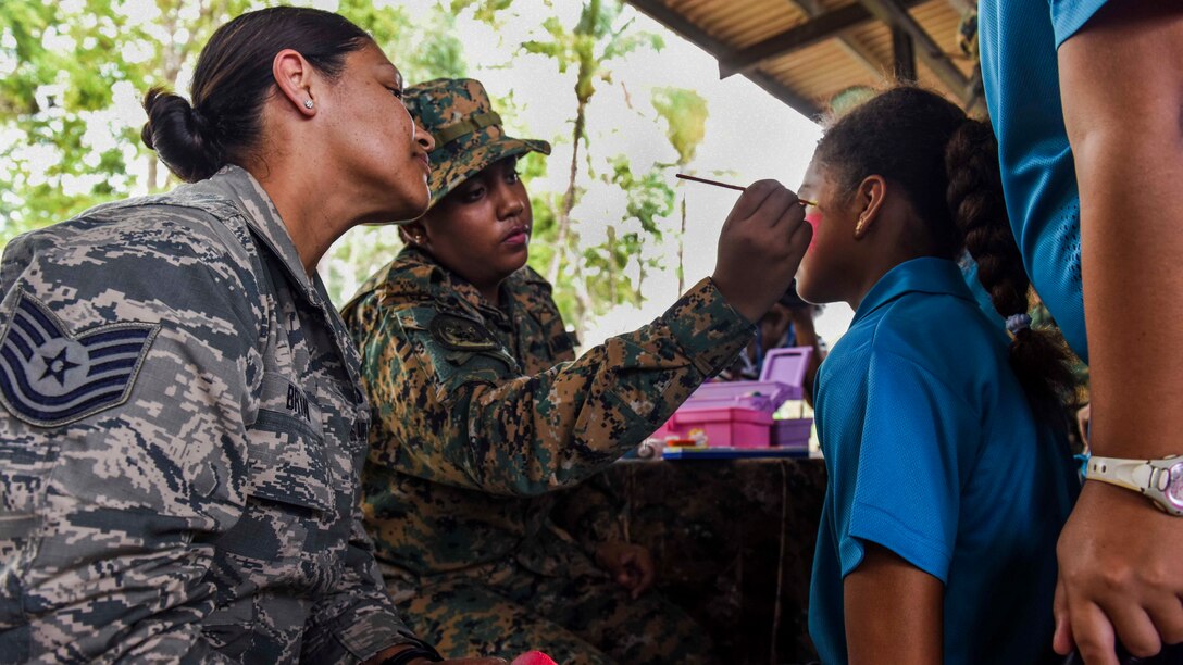An airman helps paint a face of a child.