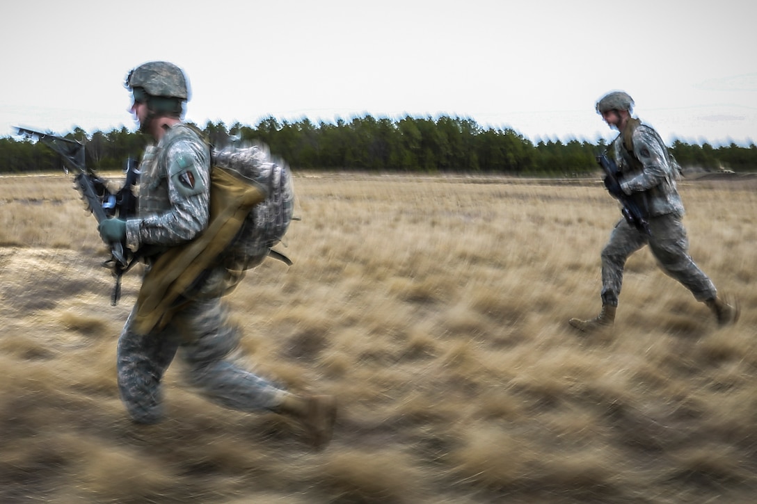 Two soldiers run through a field.