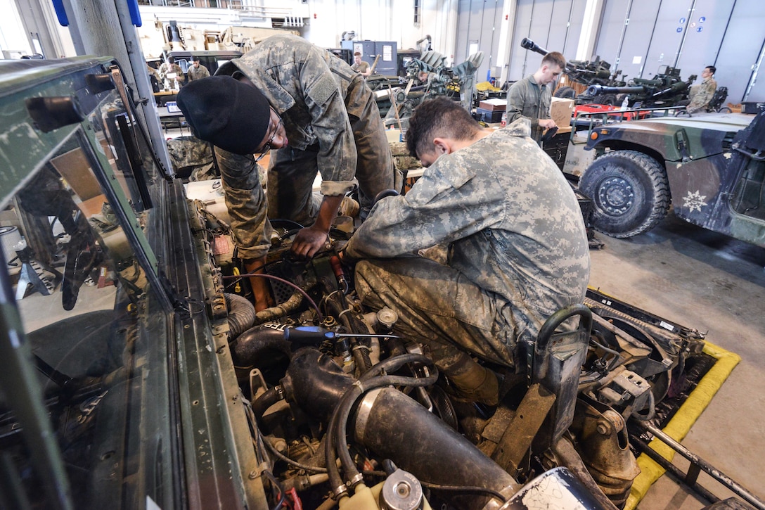 Soldiers perform maintenance on a Humvee vehicle engine.