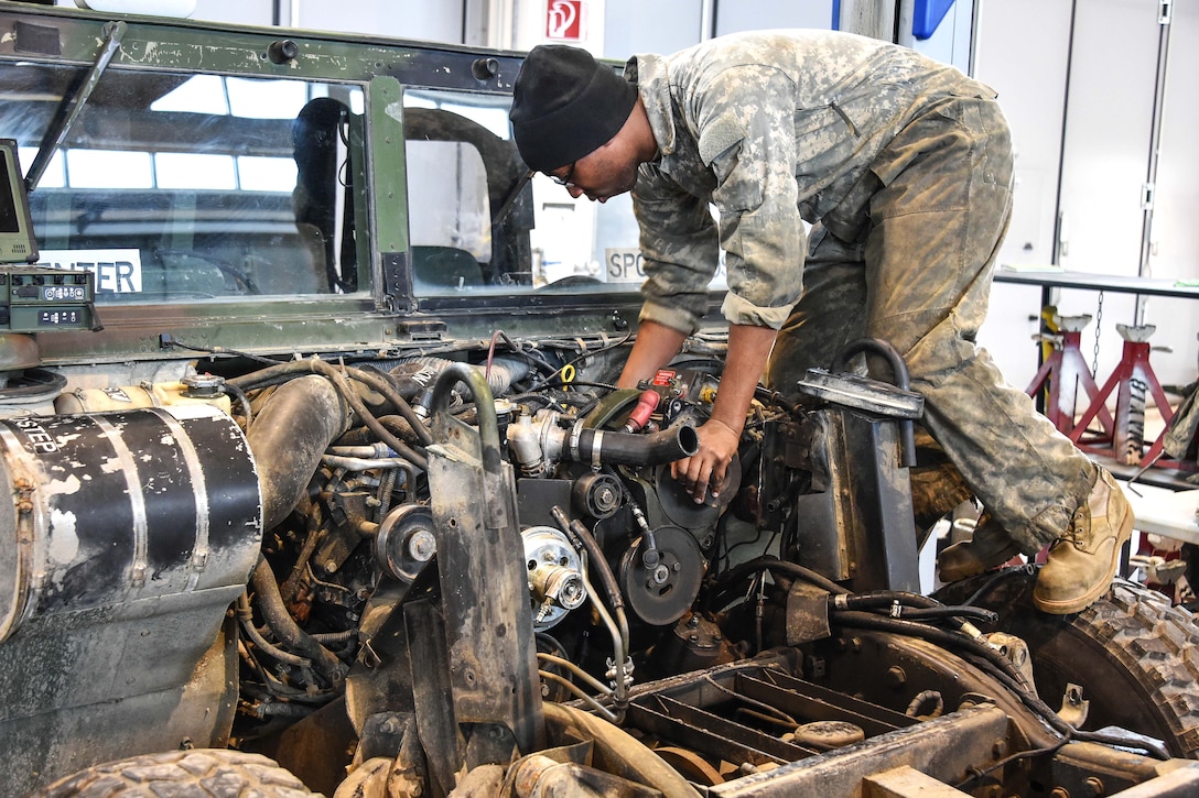 A soldier performs maintenance on a Humvee vehicle engine.