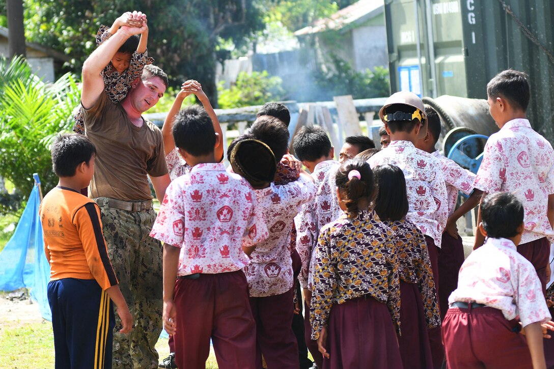 A sailor takes a break to play with students after work is completed.