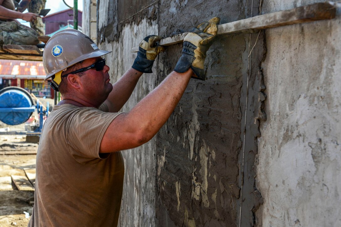A sailor applies stucco onto a wall.