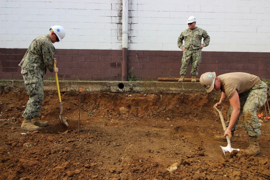 Two Navy officers begin excavation for the foundation of a classroom.