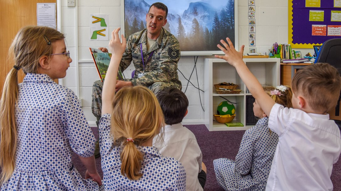 Children sit and look towards an airman reading.