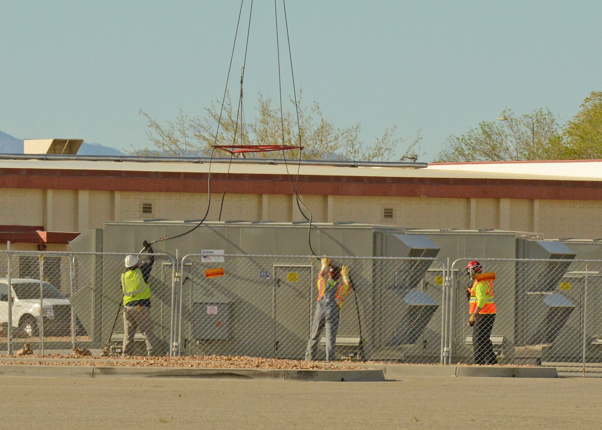 Workers from Siller Helicopters, Inc., attach cables to a new cooling unit to be lifted onto Bldg. 1600 April 7. The company's helicopter would dangle cable lines to be attached onto the old coolers, which were lifted off Bldg. 1600 and placed in a parking lot nearby. Workers then attached the cables to the new unit to be lifted onto the building. (U.S. Air Force photo by Kenji Thuloweit)