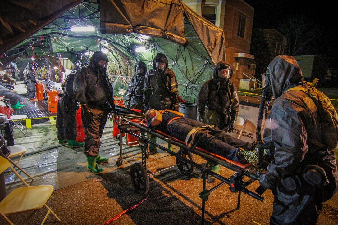 People in hazmat suits push a person on a stretcher into a tent.