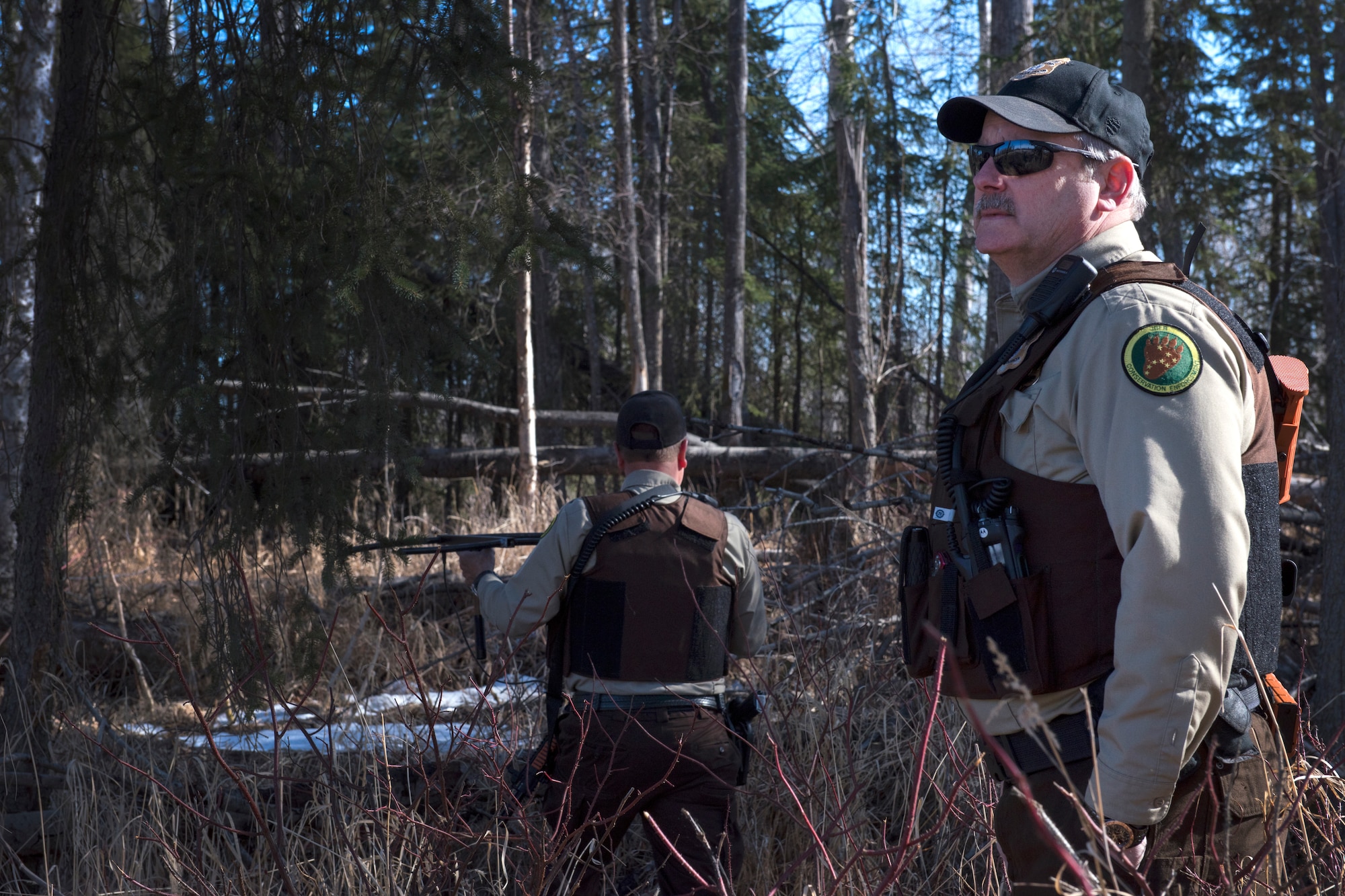 Mark Sledge, 673d Civil Engineering Squadron senior conservation law enforcement officer, and James Wendland, 673 CES chief conservation law enforcement officer, approach a black bear den at Joint Base Elmendorf-Richardson, Alaska, April 16, 2018. Making loud noises while walking the trails will alert the wildlife of your presence and reduce a surprise encounter.