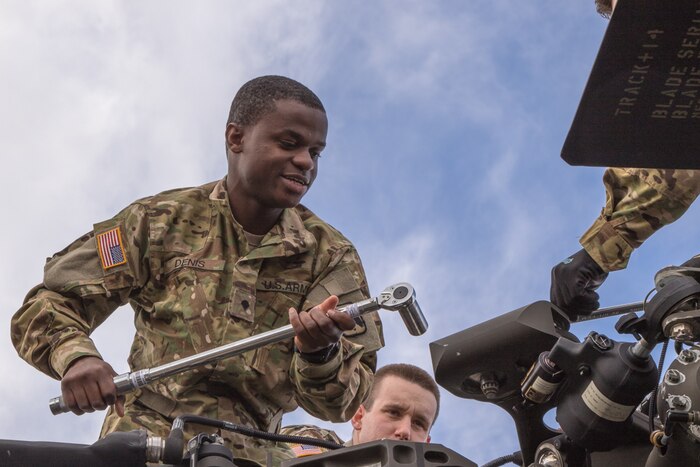 Soldier holding a large ratchet works on a helicopter.